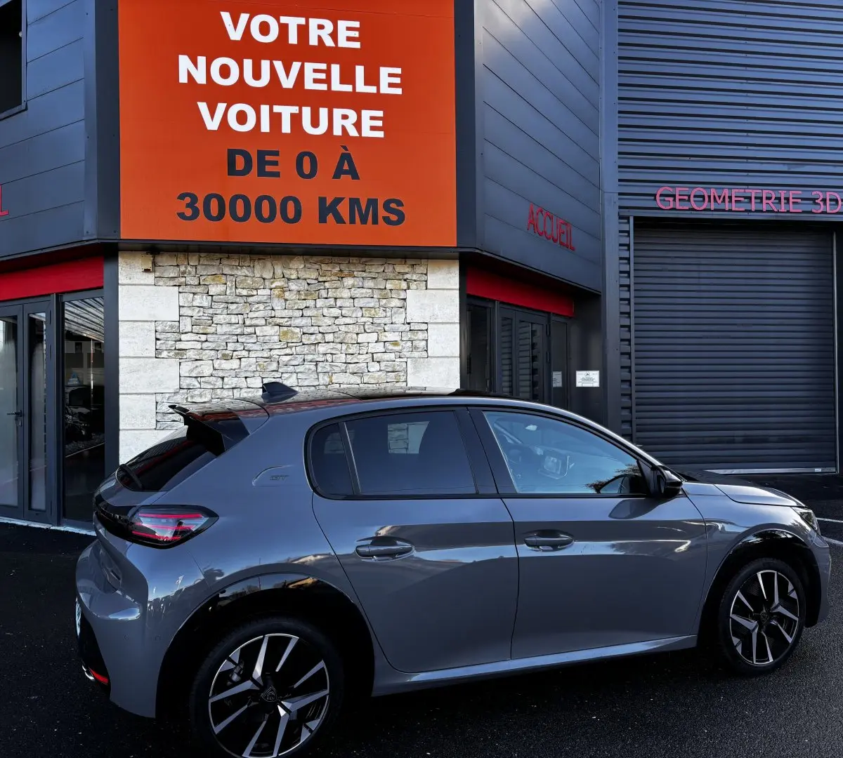 Peugeot 208 Hybrid 136 eDCS6 GT gris foncé vue de profil côté droit devant un bâtiment avec panneau orange.