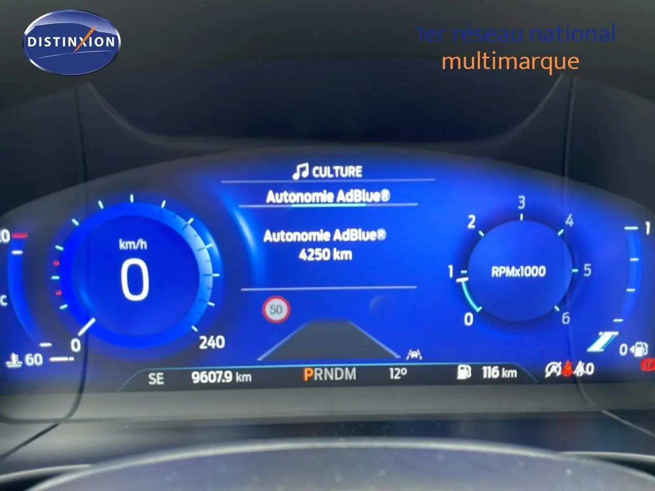 Tableau de bord numérique bleu du Ford Kuga 2024 affichant vitesse, régime moteur et autonomie AdBlue.