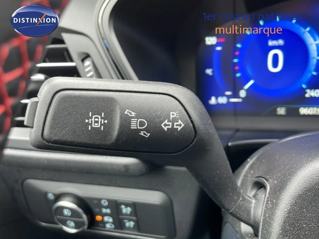 Gros plan sur le commodo gauche du tableau de bord du Ford Kuga 2024, avec affichage numérique bleu en arrière-plan.