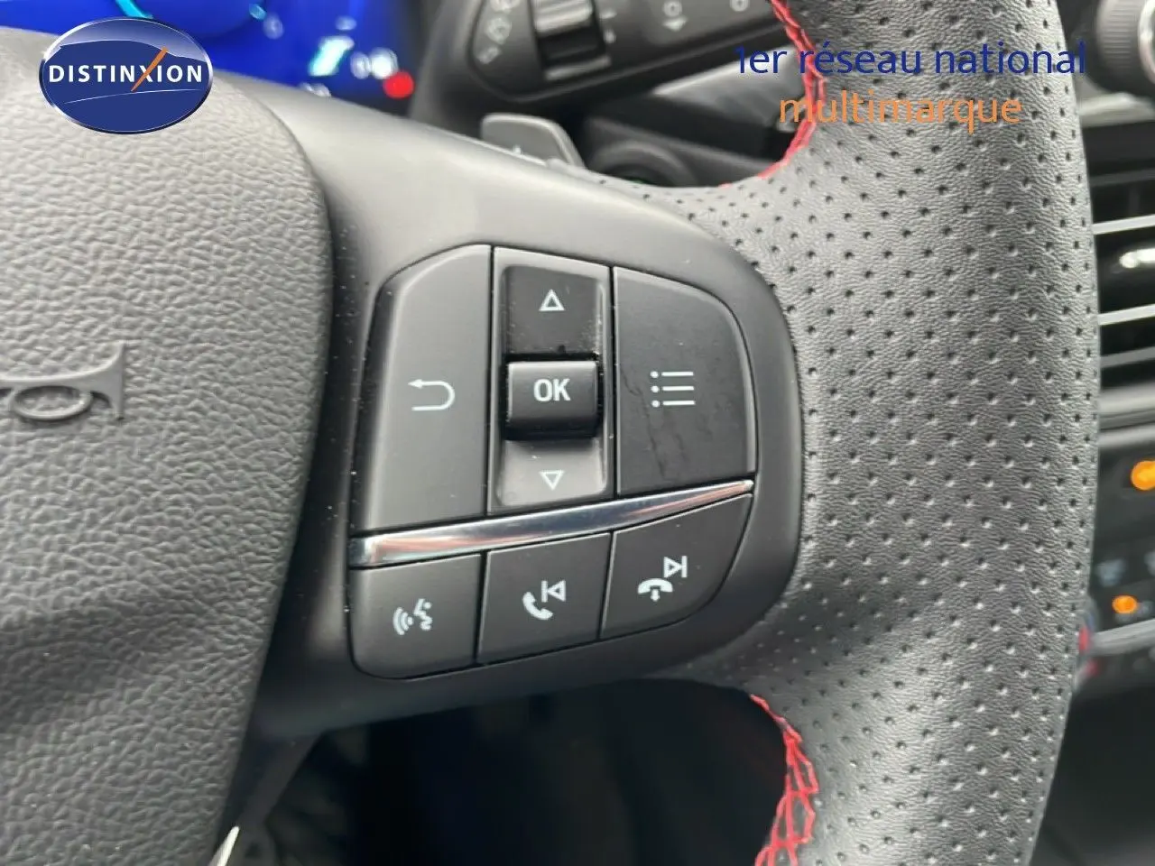 Gros plan sur le volant perforé avec surpiqûres rouges du Ford Kuga 2024 bleu Vapor Metal, mettant en valeur les commandes intégrées.