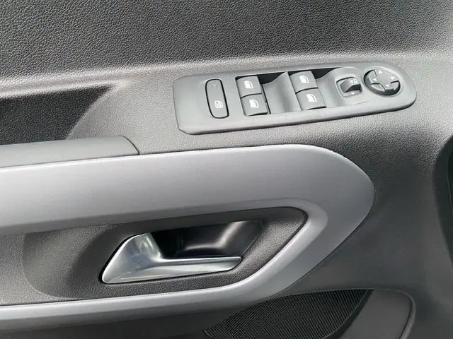 Gros plan sur la commande de lève-vitres et poignée de porte intérieure grise du Citroën Berlingo blanc 2025 côté conducteur.