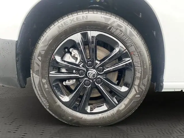 Gros plan sur la roue avant droite du Citroën Berlingo blanc, avec jante alliage noire brillante et pneu Nexen visible.