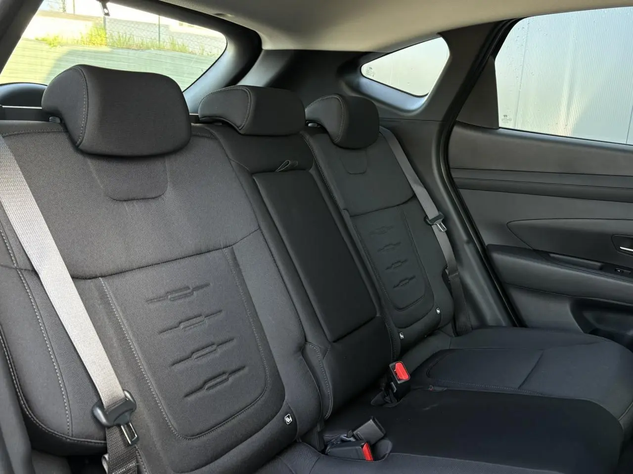 Vue intérieure des sièges arrière noirs du Hyundai Tucson 2025, avec appuie-têtes et ceintures visibles côté droit.