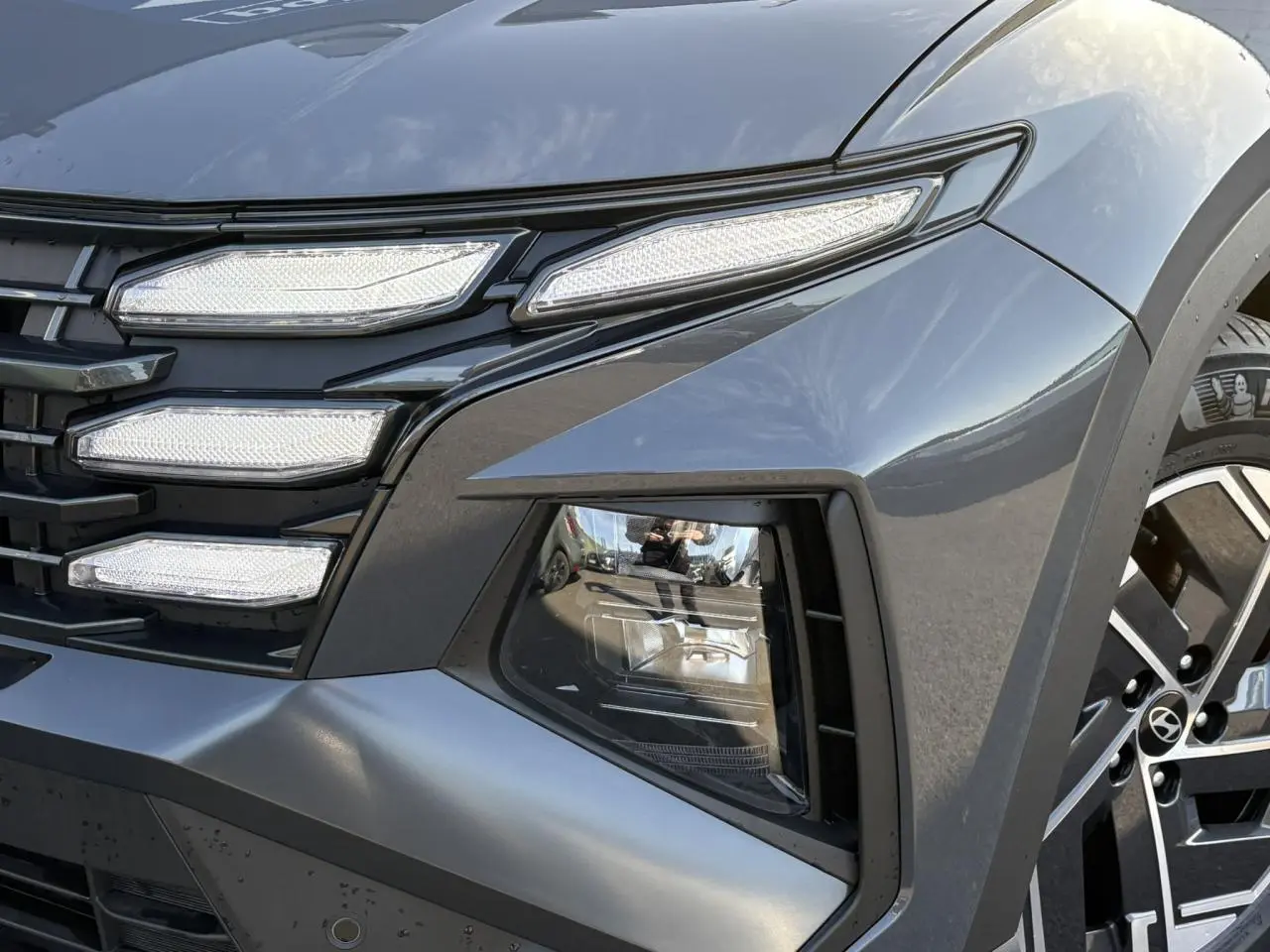 Gros plan sur le phare avant droit et la calandre du Hyundai Tucson 2025 en Ecotronic Gray métallisé.