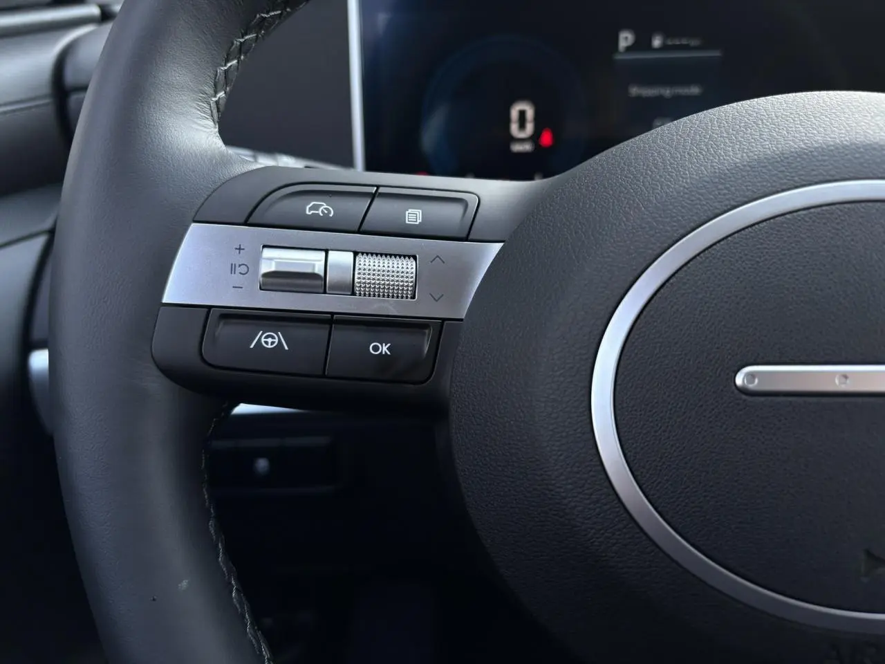 Gros plan sur les commandes gauche du volant cuir du Hyundai Tucson 2025, avec tableau de bord numérique en arrière-plan.