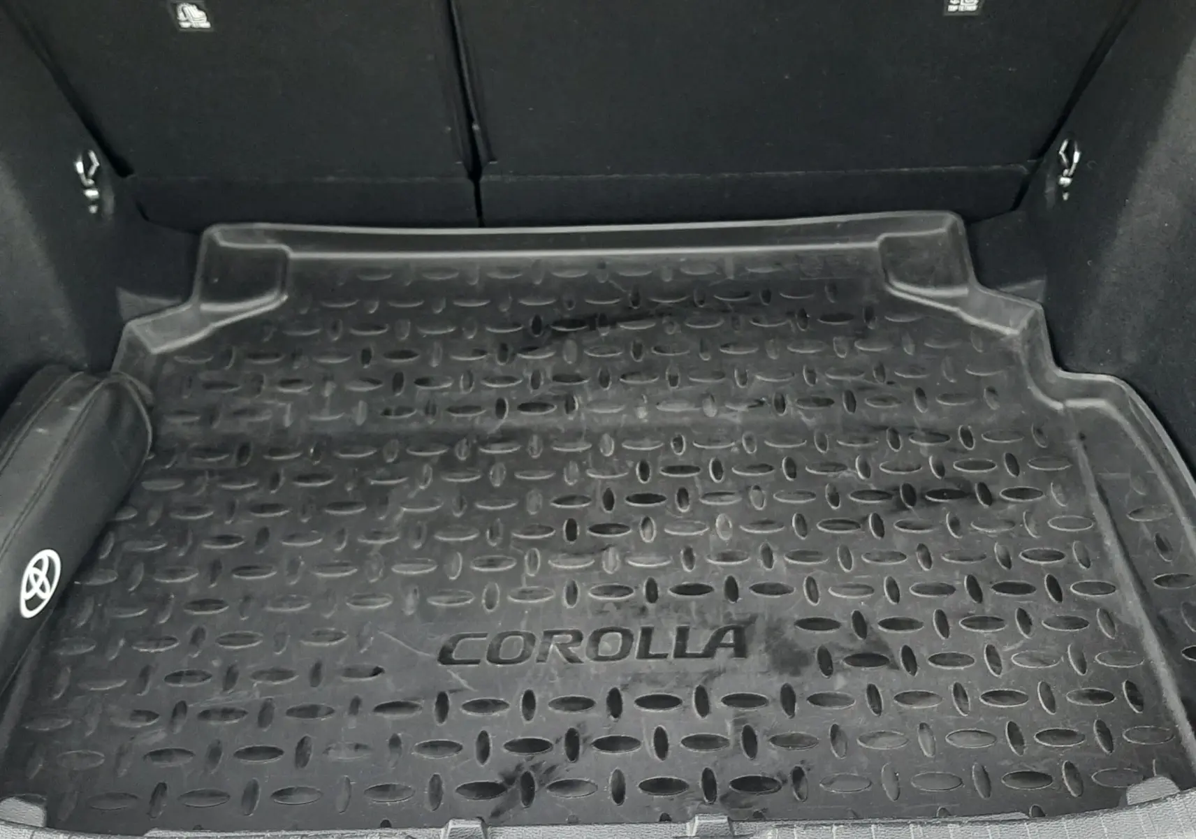 Coffre ouvert d'une Toyota Corolla blanche 2022, vue de dessus montrant le tapis de coffre noir marqué "COROLLA".