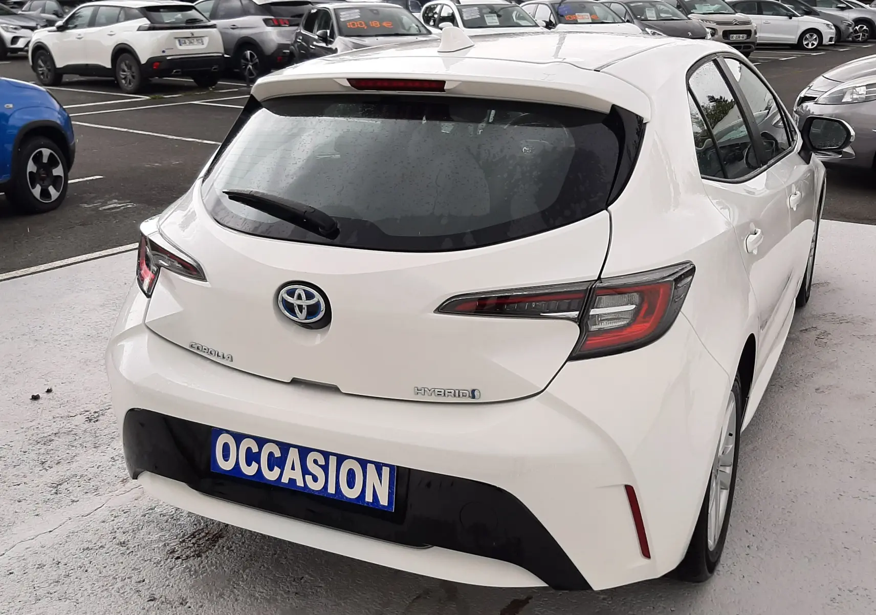 Vue 3/4 arrière droite d'une Toyota Corolla blanche hybride 2022 avec plaque "OCCASION" sur parking.