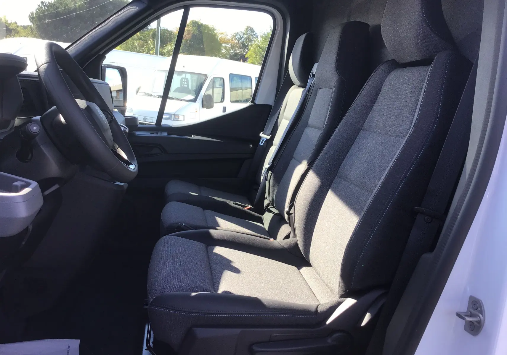 Intérieur côté conducteur du Renault Master blanc 2025, montrant les sièges gris et le volant, avec porte ouverte.