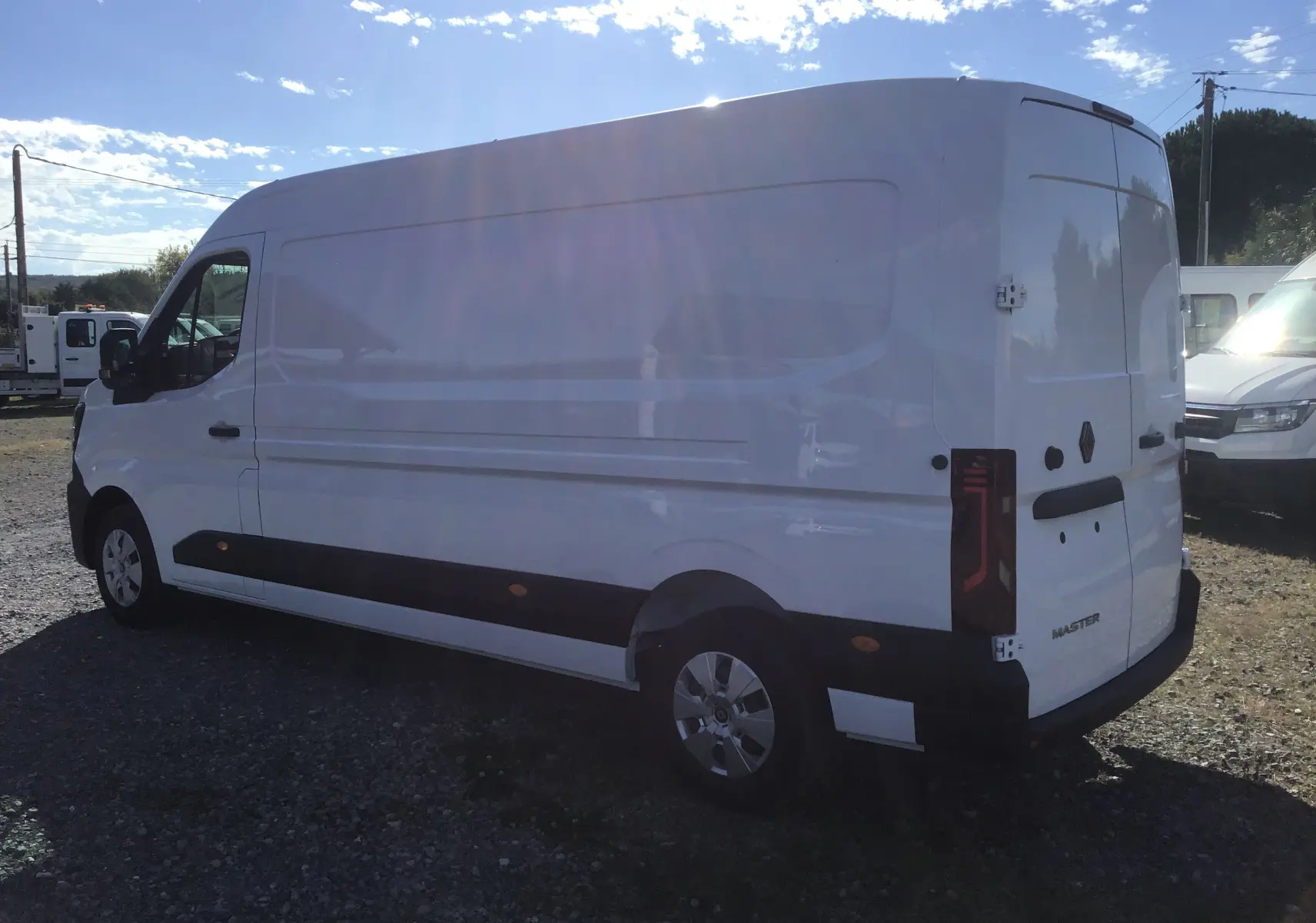 Renault Master blanc vu en 3/4 arrière côté gauche, montrant sa grande carrosserie utilitaire et ses feux arrière verticaux.