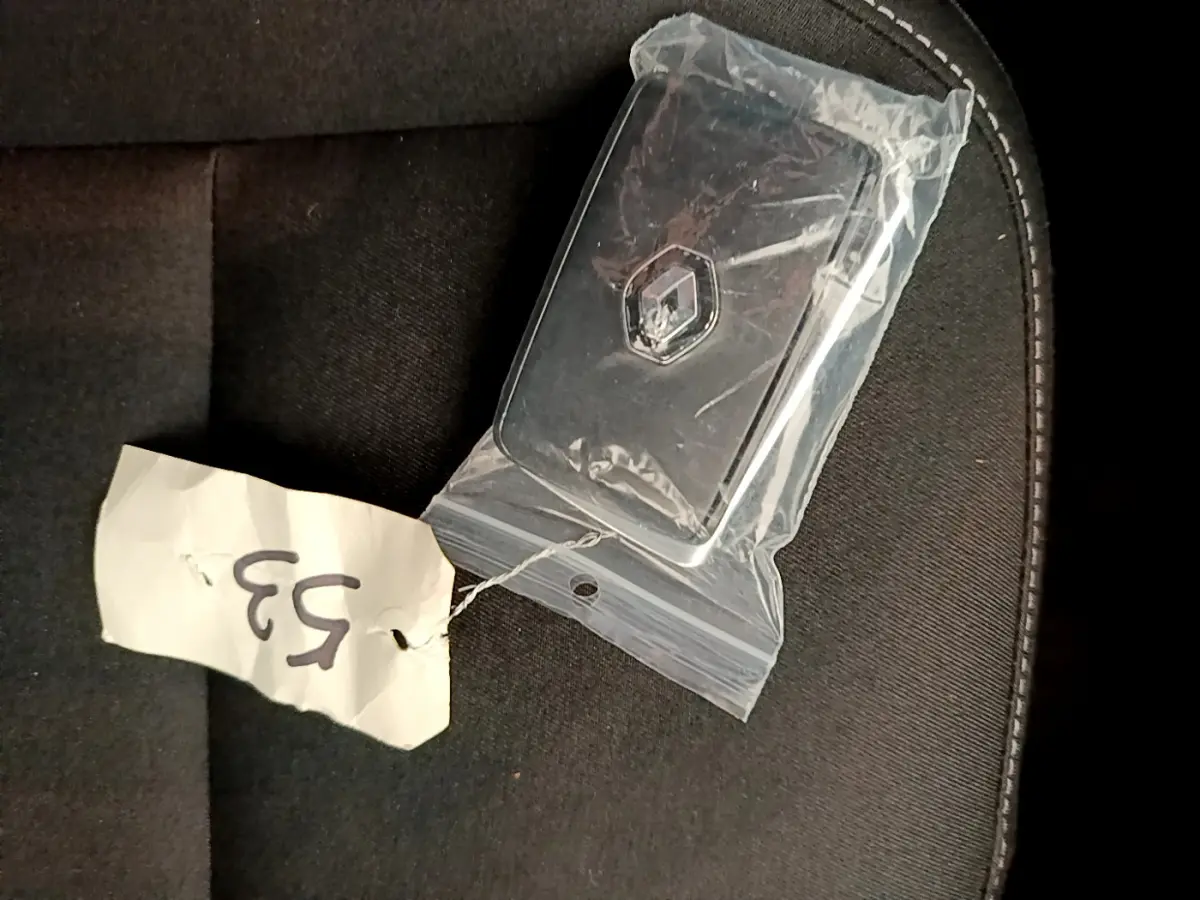Clé Renault noire sous plastique sur siège tissu noir, vue rapprochée en plongée.