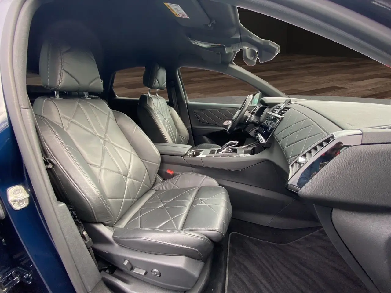 Vue intérieure côté conducteur du DS7 2024 bleu Eclipse, mettant en valeur la sellerie cuir électrique noire et le tableau de bord raffiné.