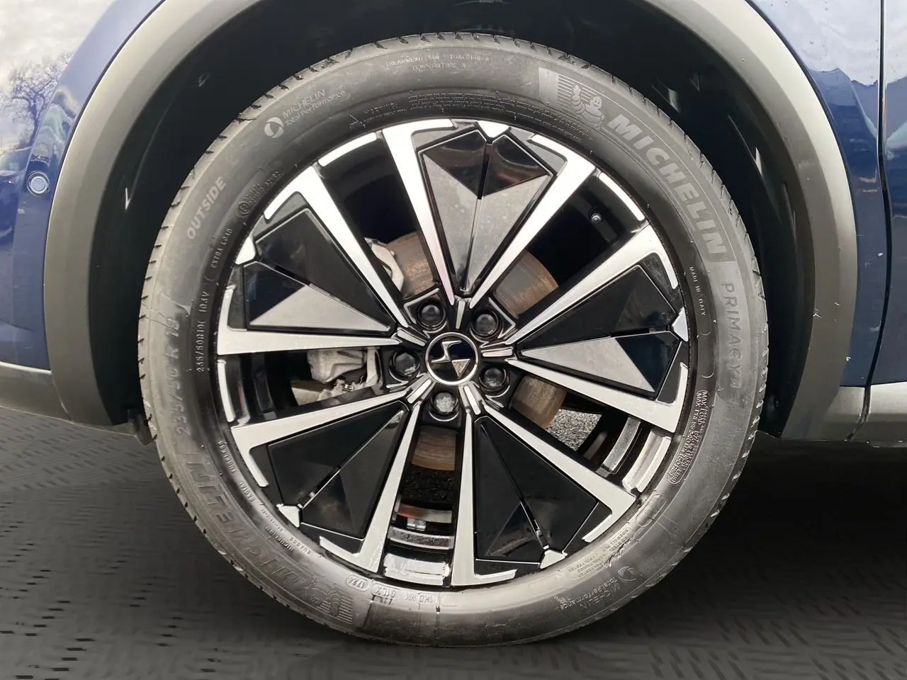 Gros plan sur la roue avant droite du DS7 Bleu Éclipse, mettant en valeur la jante alliage noire et argentée au design géométrique.