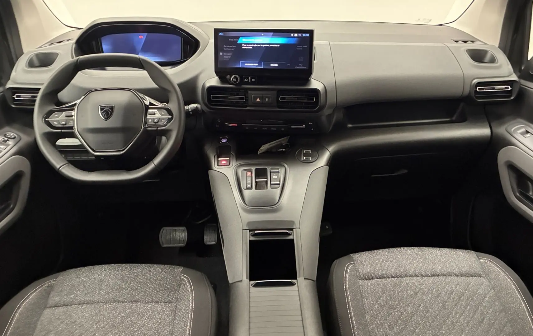 Vue intérieure avant du Peugeot Rifter 2026, tableau de bord noir avec écran tactile central et volant multifonction.