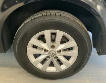 Gros plan sur la roue avant gauche d’un Volkswagen Multivan T6 noir, montrant la jante en alliage argentée et le pneu.