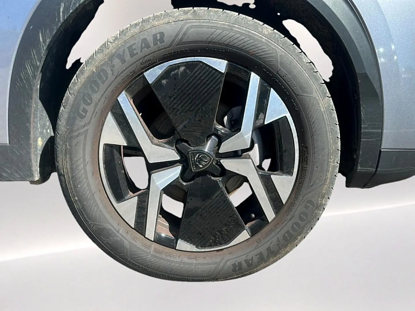 Gros plan sur la roue avant gauche d’un Peugeot 2008 gris Artense avec jante alu bicolore et pneu Goodyear.