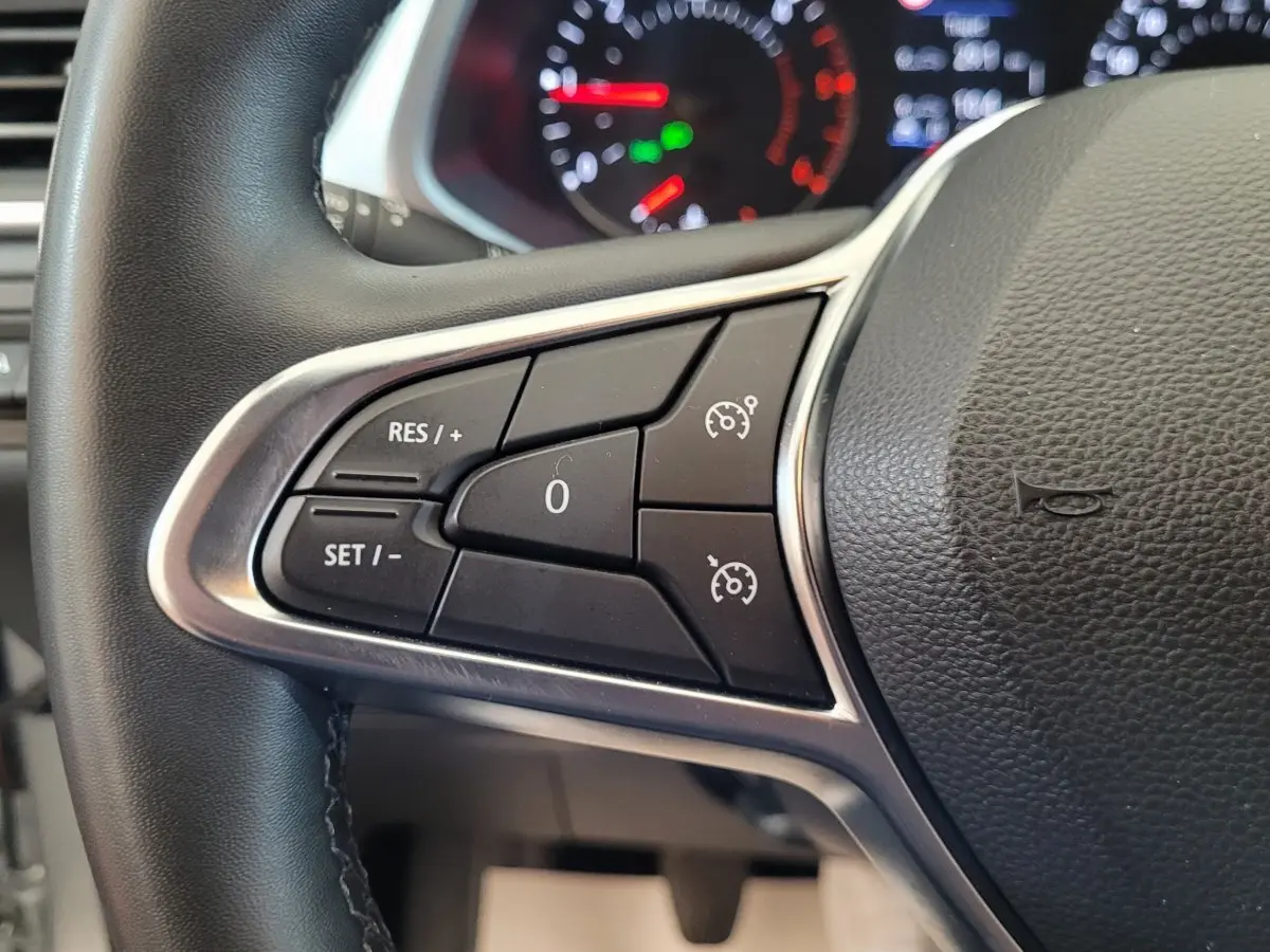 Gros plan sur les commandes au volant gauche du Renault Captur Business gris clair, avec tableau de bord lumineux en arrière-plan.