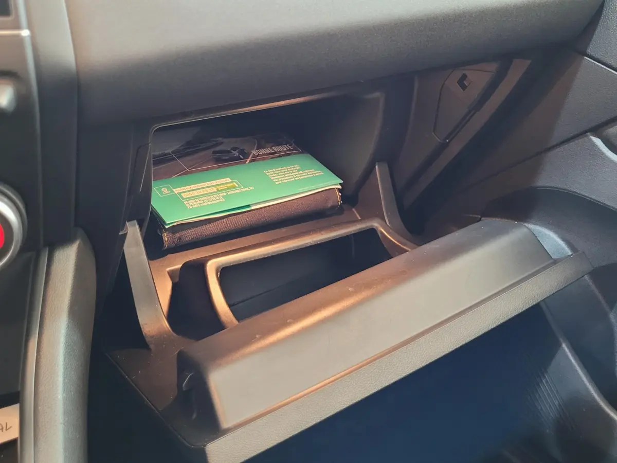 Gros plan sur la boîte à gants ouverte du Renault Captur Business gris clair, montrant un manuel et un espace de rangement intérieur.