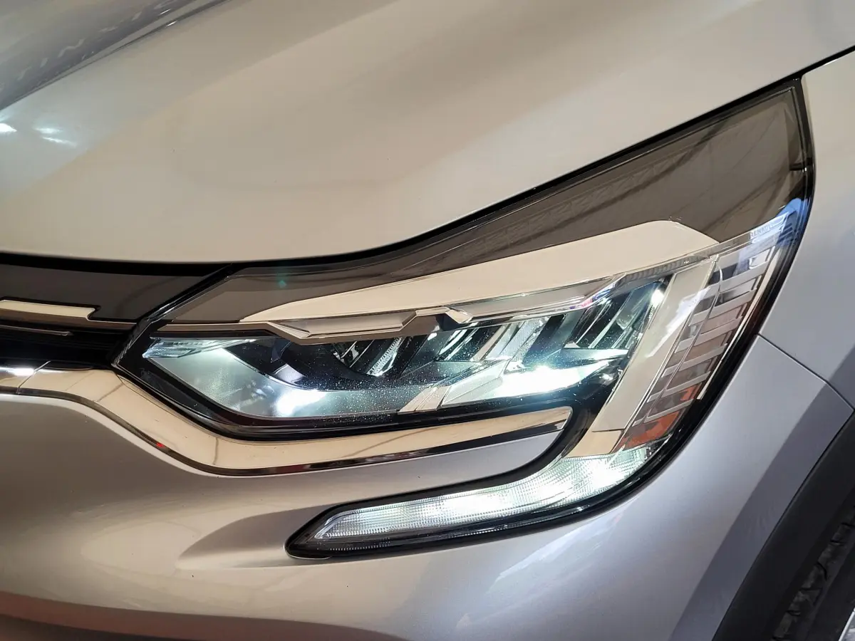 Gros plan sur le phare avant droit allumé d'un Renault Captur gris clair 2021, soulignant ses LED modernes.