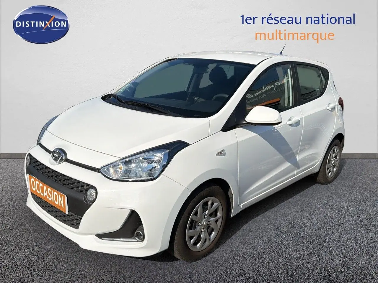 Vue 3/4 avant droite d'une Hyundai i10 blanche de 2018 avec calandre noire et jantes alliage.