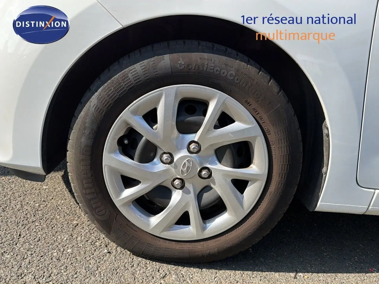 Gros plan sur la roue avant droite d'une Hyundai i10 blanche de 2018 avec jante argentée et logo Hyundai visible.