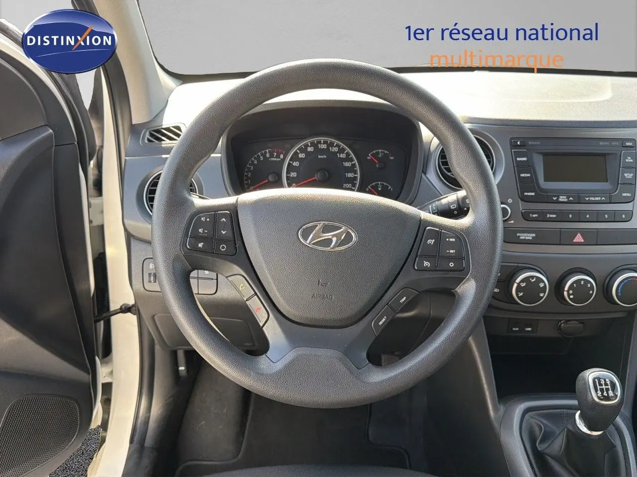Vue centrée sur le volant Hyundai i10 blanche 2018 avec tableau de bord et levier de vitesses manuel visible.