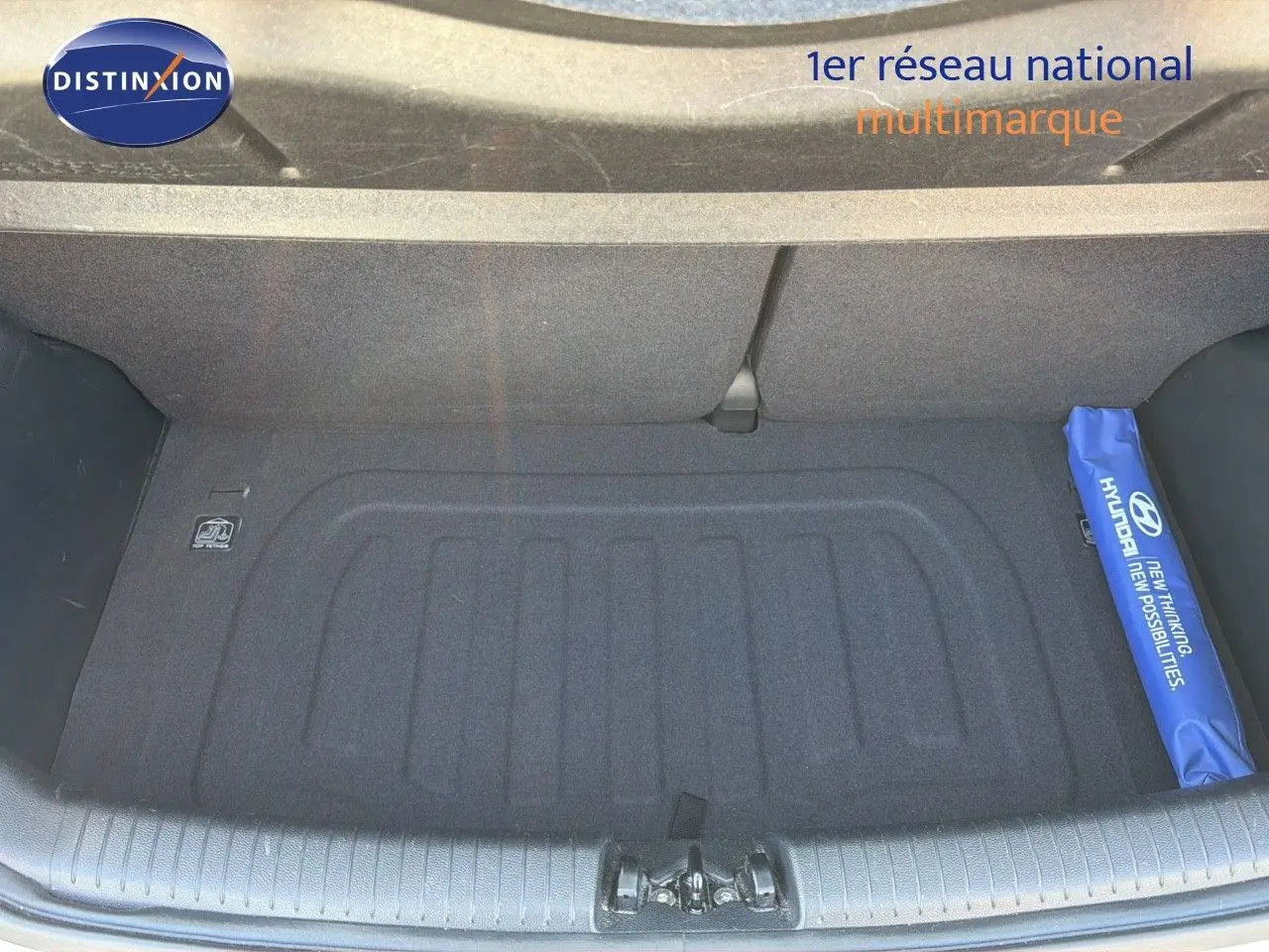 Coffre ouvert d'une Hyundai i10 blanche, vue de dessus, avec tapis de coffre noir et trousse bleue Hyundai sur le côté droit.