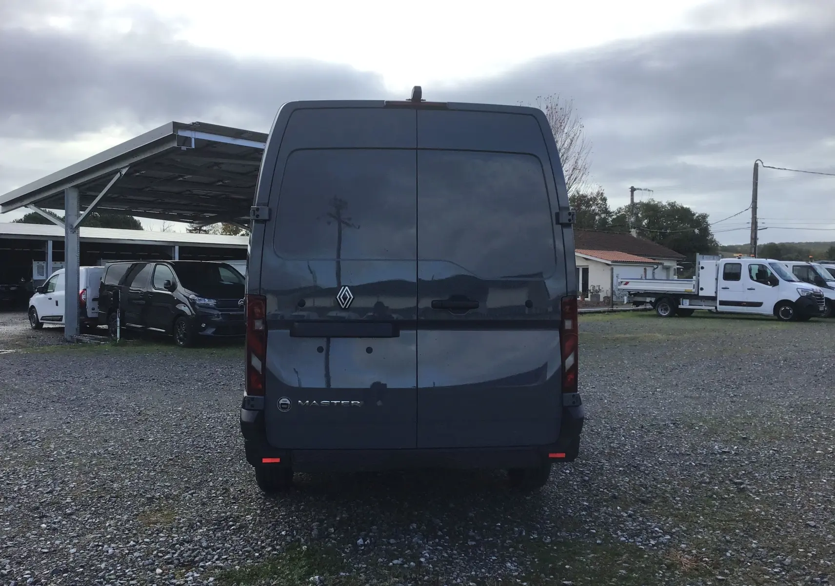 Vue arrière d’un Renault Master L3H2 gris urbain 2025, avec portes arrière fermées sur un sol gravillonné.