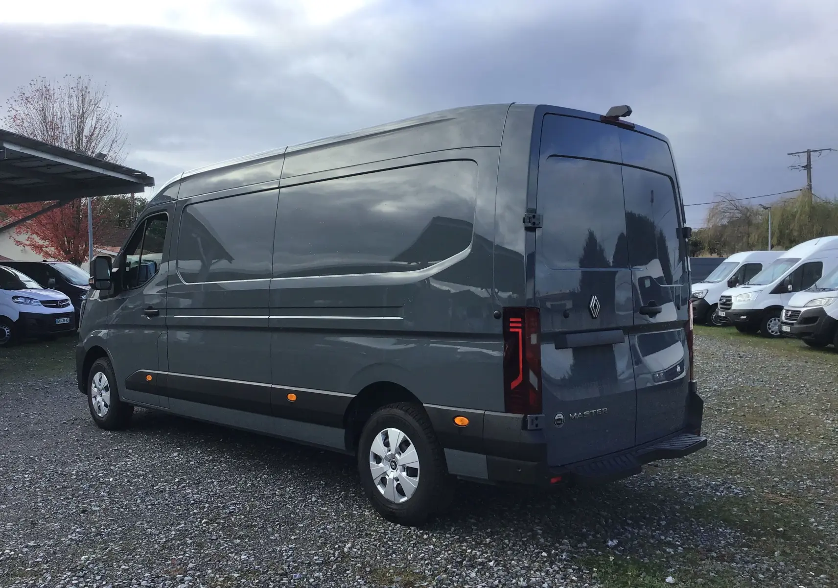 Vue 3/4 arrière droite d’un Renault Master gris urbain avec feux arrière LED et marchepied arrière visible.
