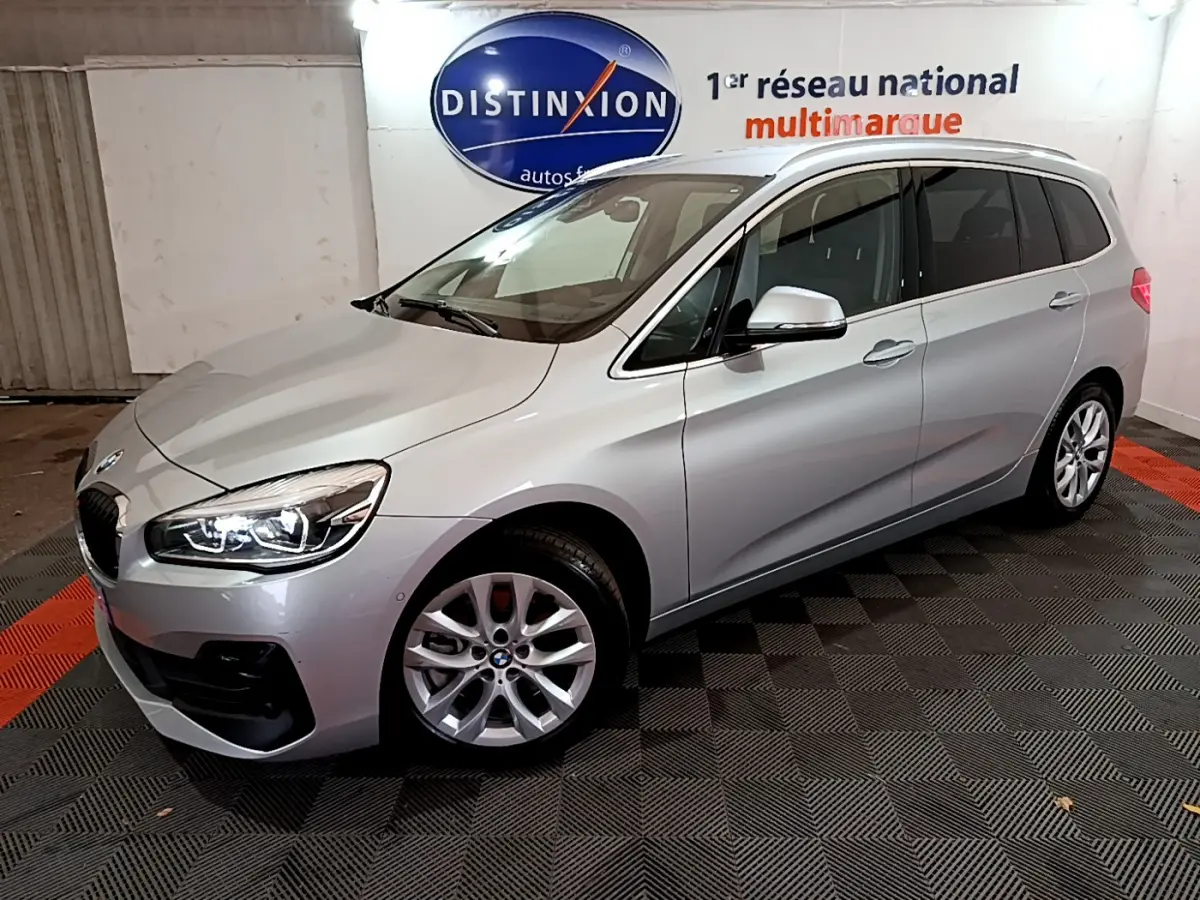BMW Série 2 Gran Tourer 218d gris clair vue 3/4 avant droit avec phares LED allumés en intérieur showroom.