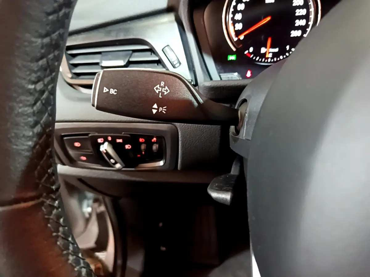 Gros plan sur la manette de clignotants et commandes d’éclairage du tableau de bord d’une BMW Série 2 Gran Tourer gris clair.