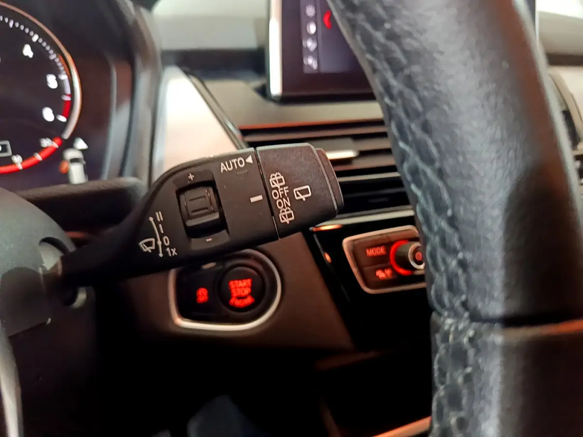 Détail intérieur du volant cuir noir de la BMW Série 2 Gran Tourer 218d, avec commande essuie-glace et bouton start/stop rouge.