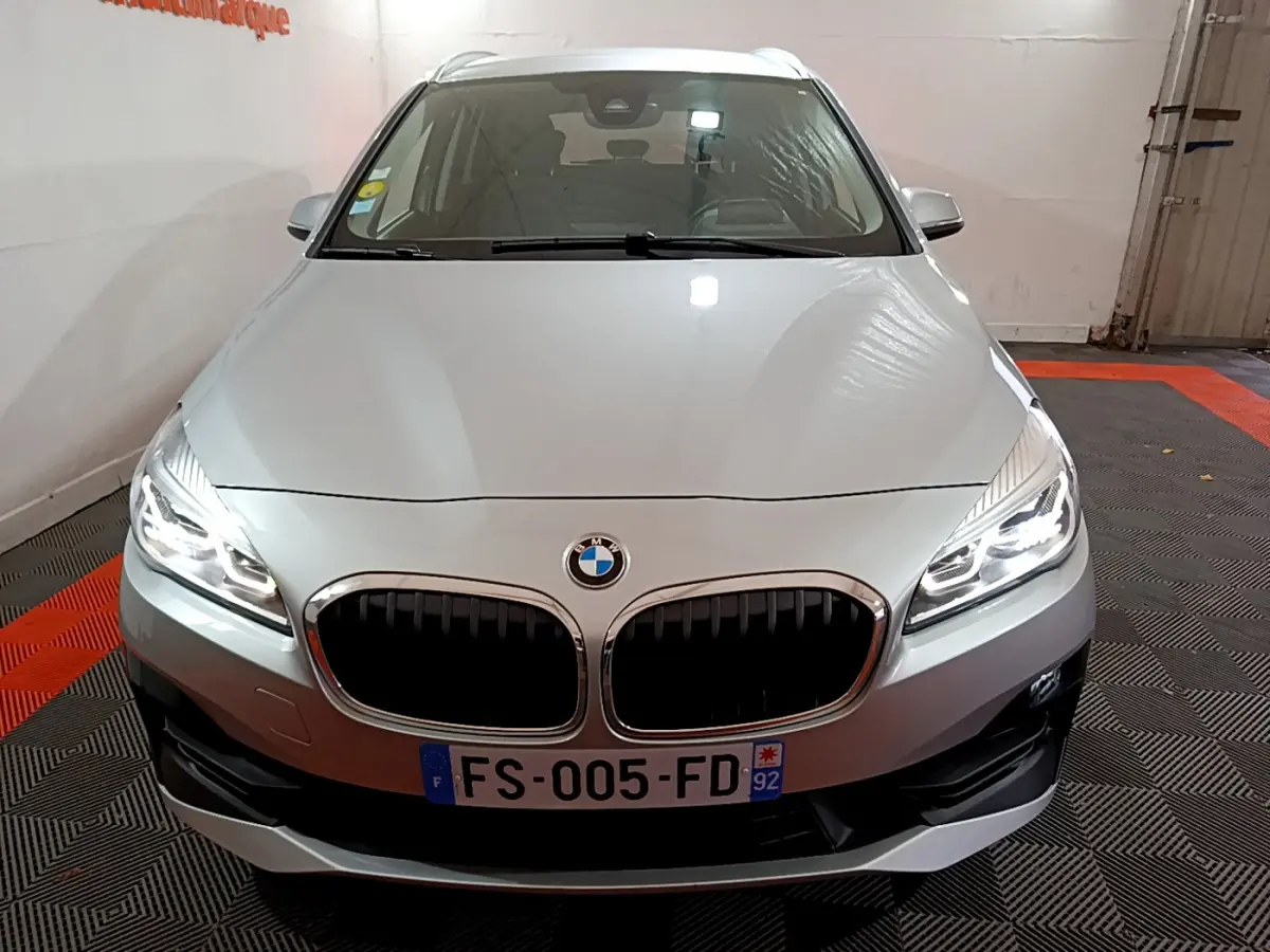 BMW Série 2 Gran Tourer gris clair vue de face avec phares LED allumés dans un garage.