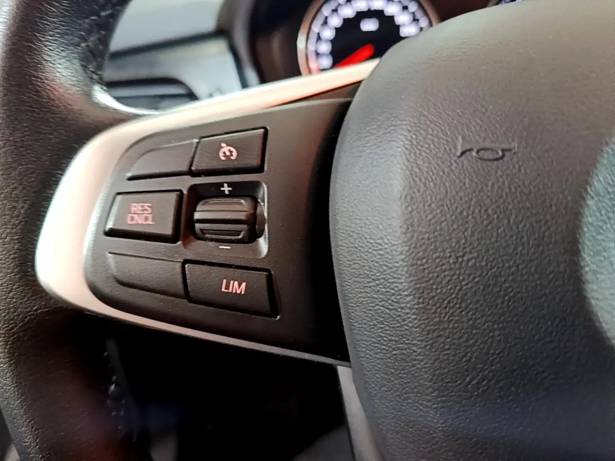 Gros plan sur les commandes du volant à gauche d'une BMW Série 2 Gran Tourer gris clair, boutons de régulateur de vitesse visibles.