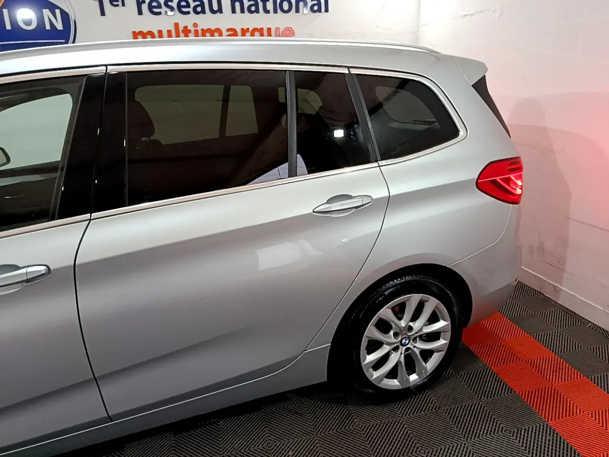 Vue latérale droite sur l'arrière d'une BMW Série 2 Gran Tourer 218d gris clair avec feux arrière allumés.
