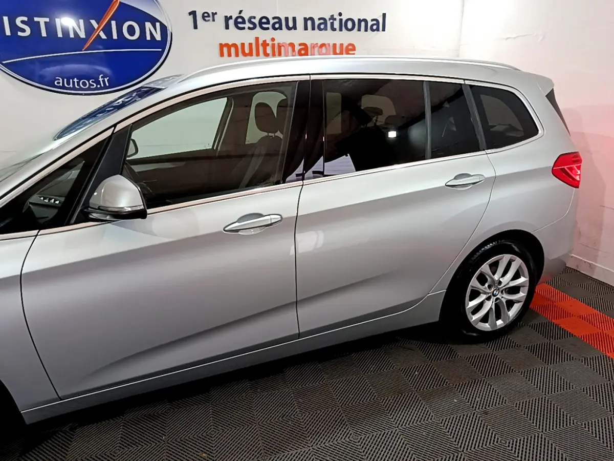 Profil côté gauche d'une BMW Série 2 Gran Tourer 218d Lounge gris clair, mettant en valeur ses vitres teintées et ses jantes alliage.