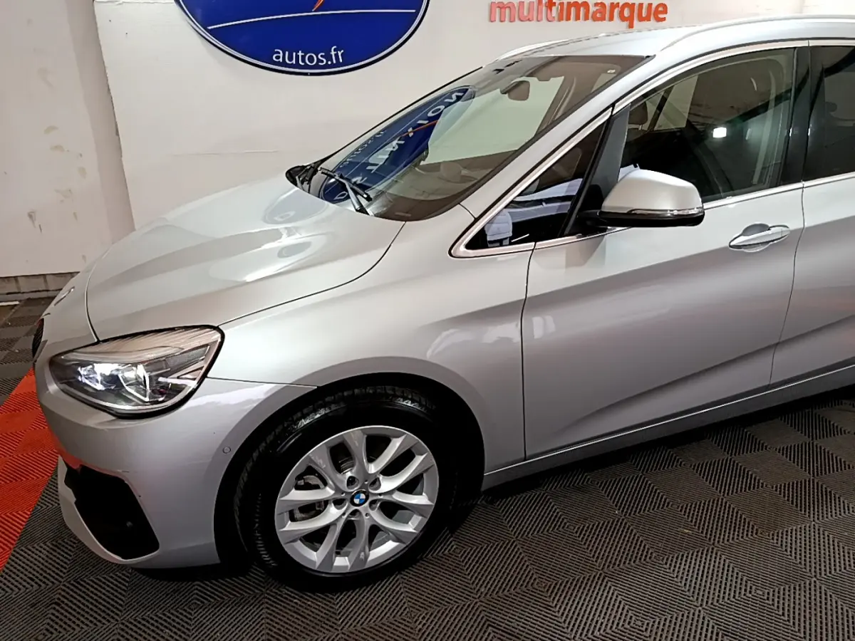 Vue 3/4 avant gauche d'une BMW Série 2 Gran Tourer 218d Lounge gris clair avec jantes alliage et rétroviseur argenté.