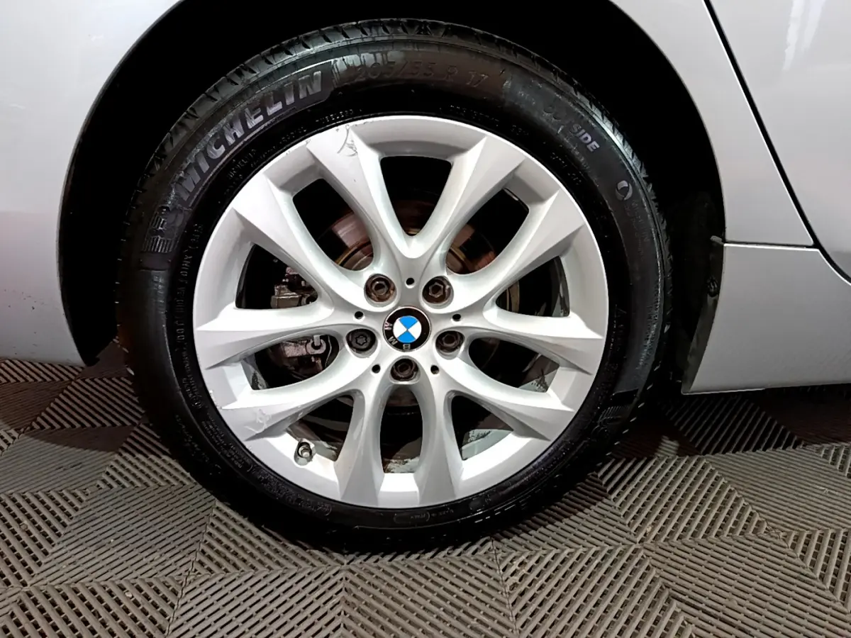 Gros plan sur la roue avant droite d'une BMW Série 2 Gran Tourer 218d gris clair avec jante alliage et logo BMW central.