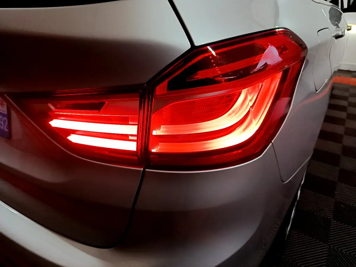 Gros plan sur le feu arrière droit rouge allumé d'une BMW Série 2 Gran Tourer F46 gris clair, vue arrière latérale.