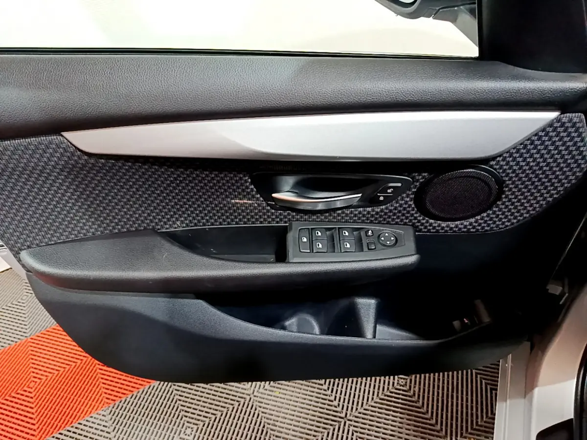 Gros plan sur la porte avant gauche de la BMW Série 2 Gran Tourer gris clair, avec commandes de vitres et haut-parleur intégré.