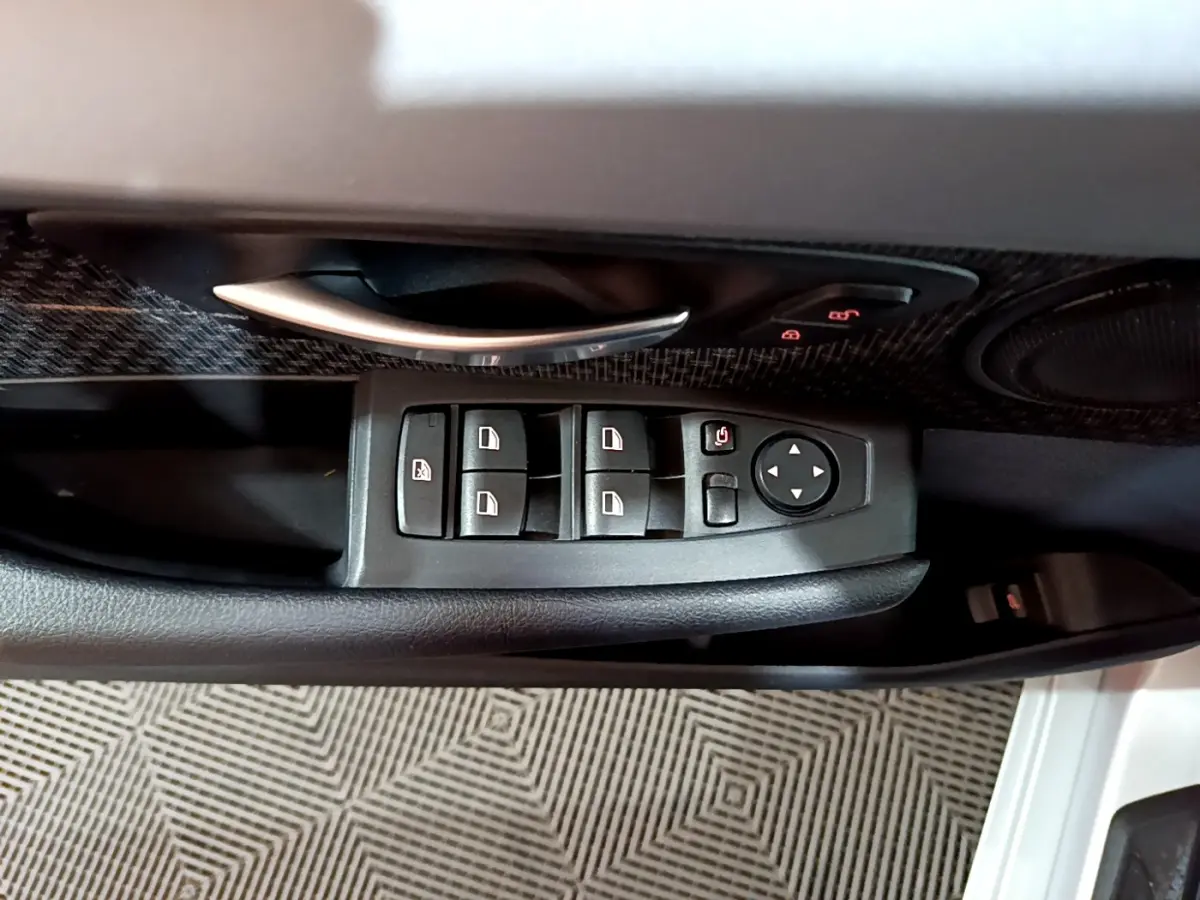 Gros plan sur les commandes des vitres et la poignée intérieure côté gauche d'une BMW Série 2 Gran Tourer gris clair.