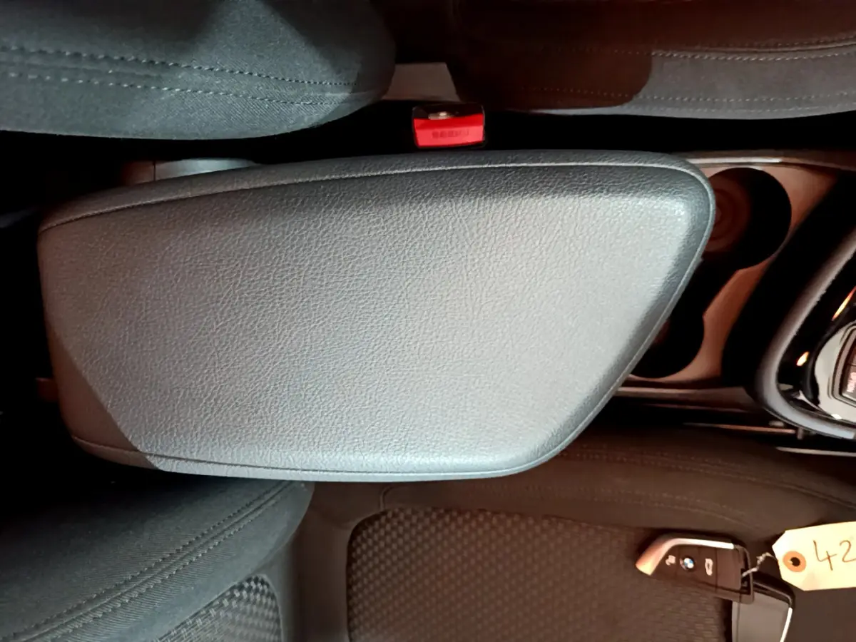 Vue rapprochée de l'accoudoir central gris clair et de la clé BMW posée sur le siège avant noir d'une Série 2 Gran Tourer F46.