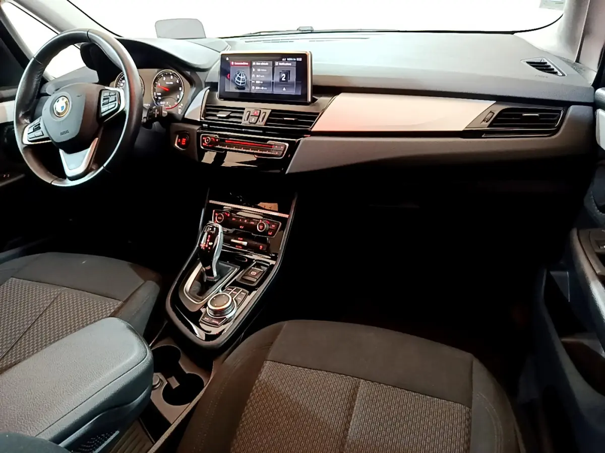 Vue intérieure avant de la BMW Série 2 Gran Tourer 218d Lounge, tableau de bord noir avec écran central et volant cuir.