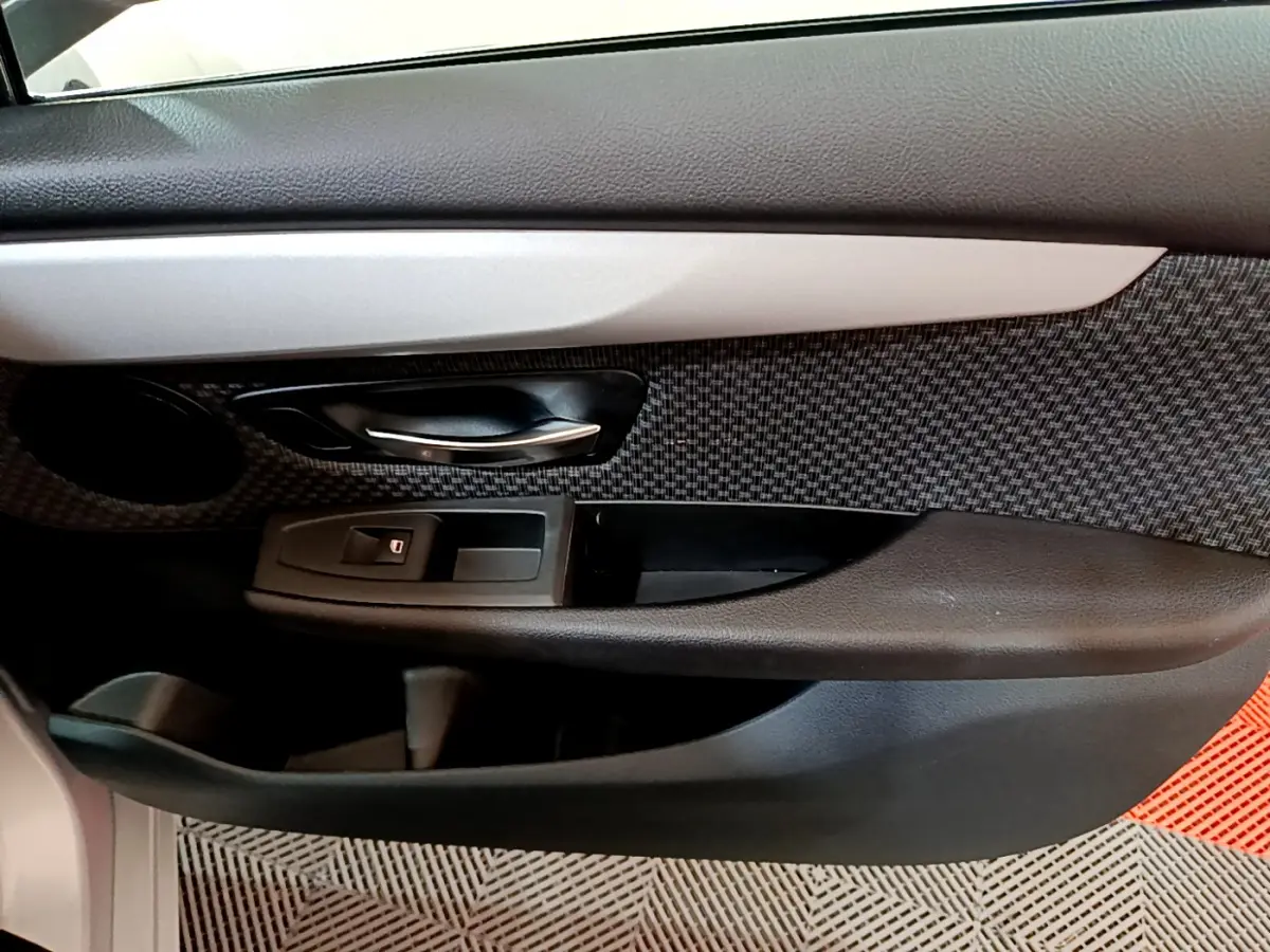 Gros plan sur la porte côté conducteur de la BMW Série 2 Gran Tourer gris clair, avec poignée alu et habillage tissu à motifs.