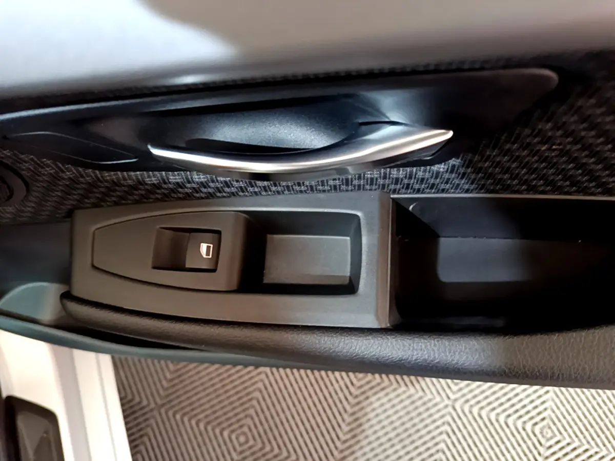 Gros plan sur la poignée intérieure et le bouton de lève-vitre côté conducteur d'une BMW Série 2 Gran Tourer gris clair.