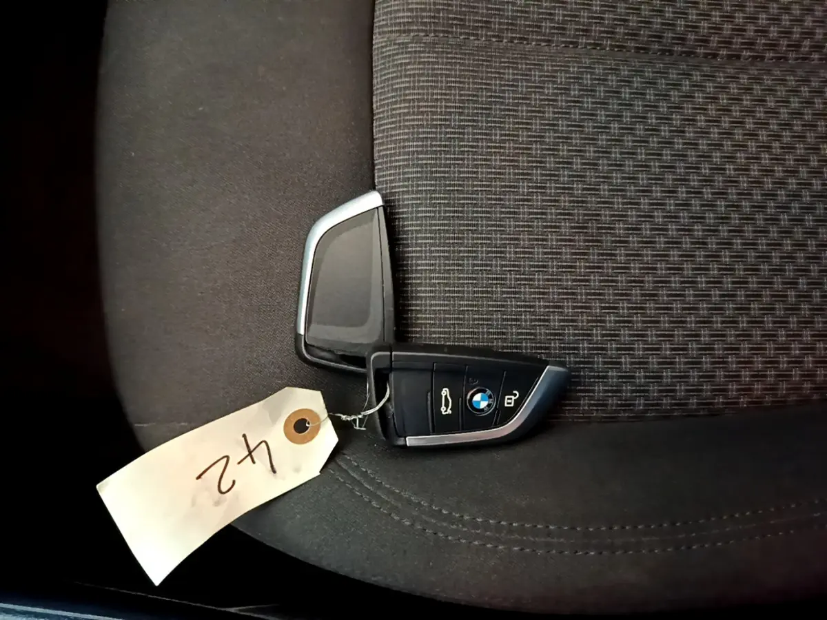 Clé BMW posée sur un siège tissu gris foncé à motifs, avec étiquette blanche numérotée "42".