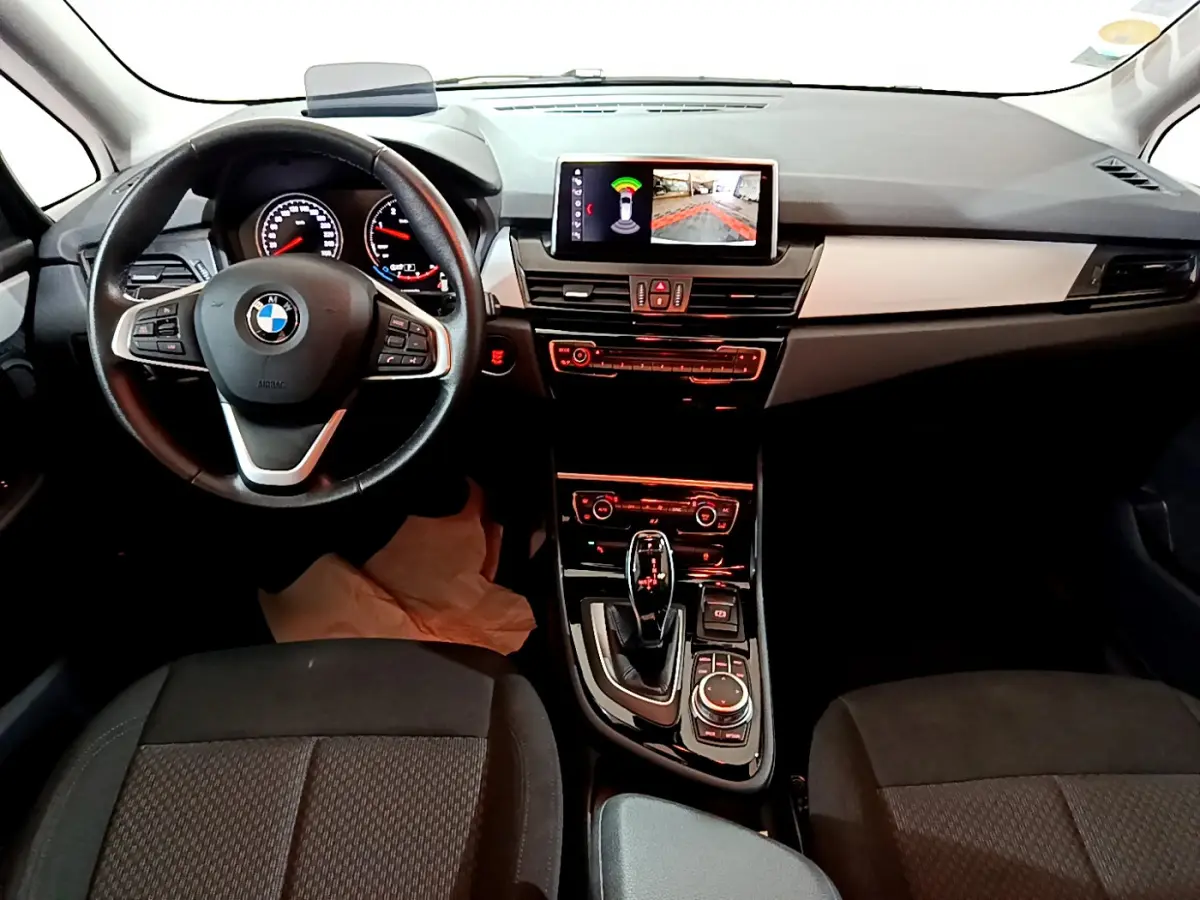 Vue intérieure avant de la BMW Série 2 Gran Tourer 218d Lounge, tableau de bord et volant cuir noir avec écran central.