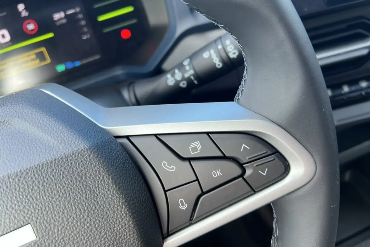 Gros plan sur les commandes au volant cuir côté droit du Dacia Bigster Hybrid 155 Expression Plus, avec écran numérique en arrière-plan.