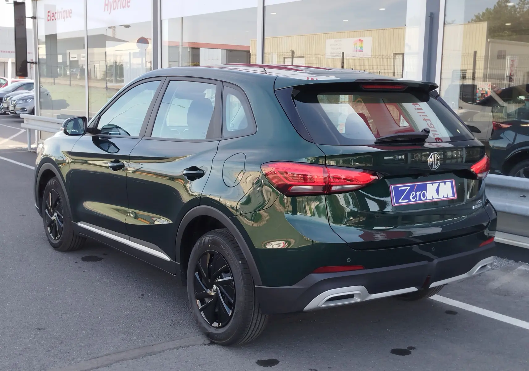 Vue 3/4 arrière droite du SUV MG ZS Emerald Green Metal avec jantes noires et détails chromés au parking d’un concessionnaire.