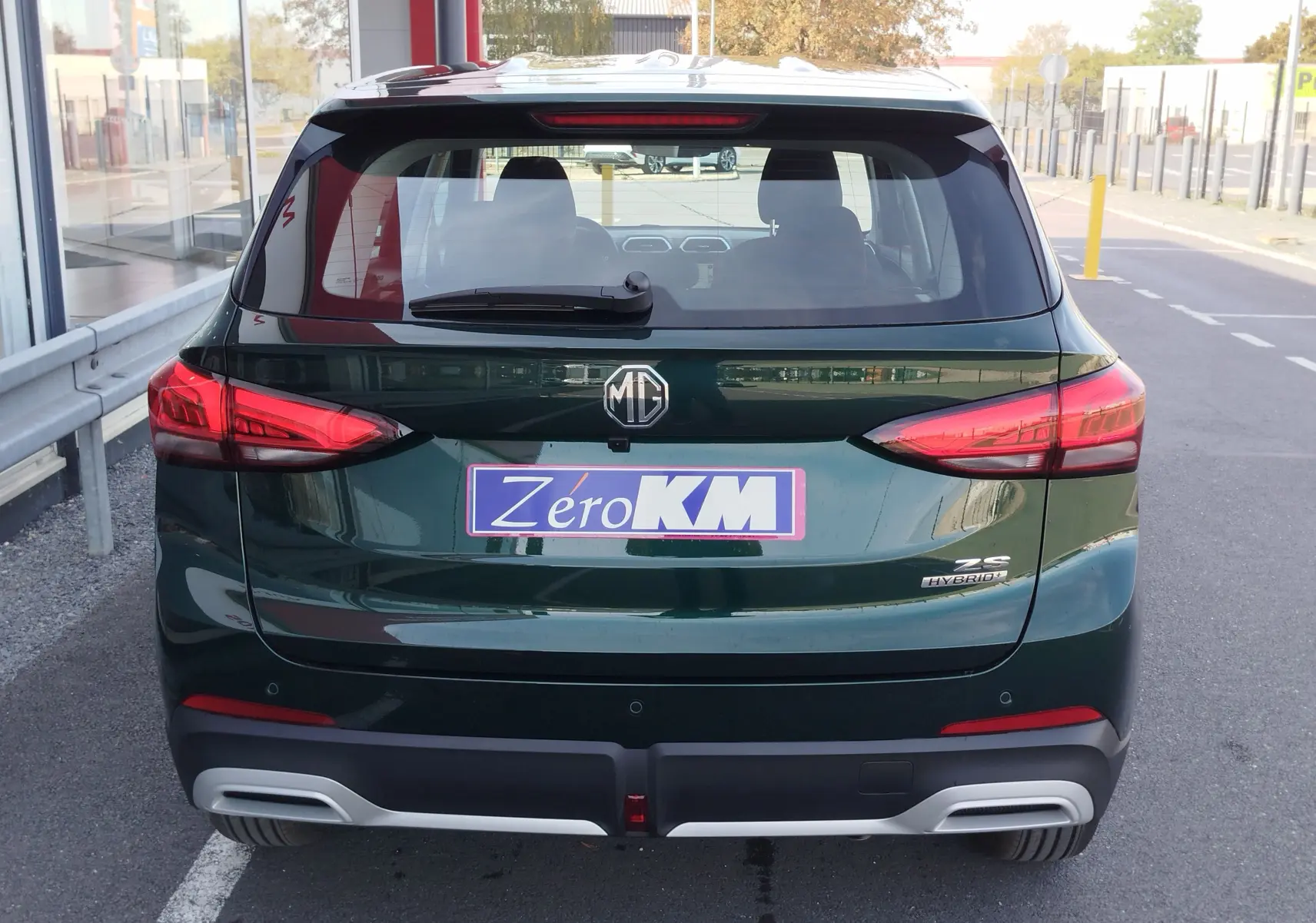 Vue arrière d’un MG ZS hybride vert émeraude avec feux LED et logo MG bien visibles sur un parking extérieur.
