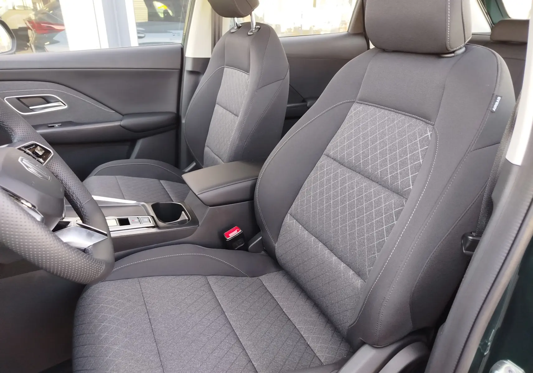 Vue intérieure côté gauche du MG ZS 2026, sièges tissu gris avec surpiqûres et volant cuir perforé.